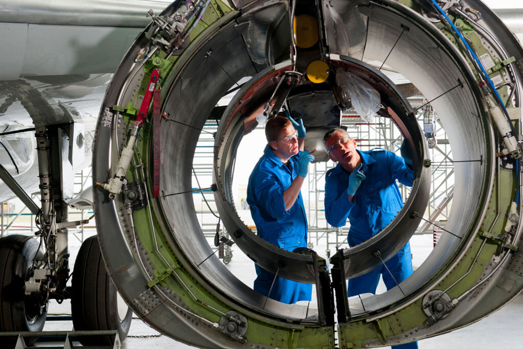 Engineers in uniforms inspecting the engine casing of a passenger jet at a hangar