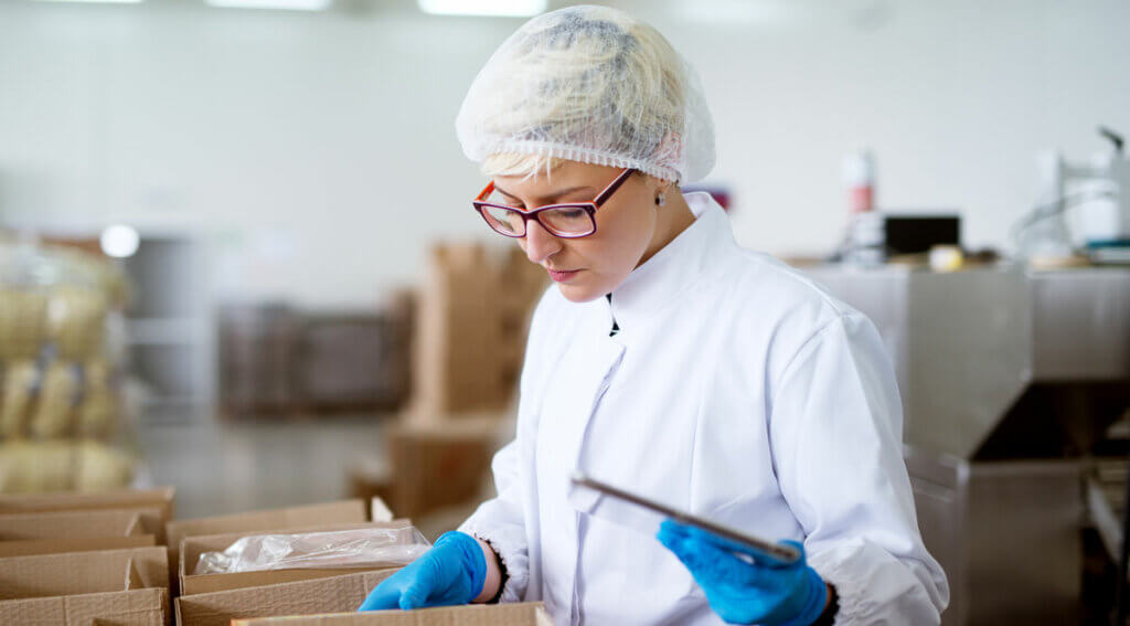 Worker-in-sterile-cloths-using-a-tablet-to-check-correction-of-inventory-within-boxes-in-factory-storage-room
